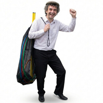 Homme souriant portant un bonnet et une chemise blanche, avec un sac en filet rempli d’accessoires colorés, prêt pour le kit d’initiation pétanque.