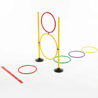 Kit d’initiation pétanque : deux poteaux jaunes sur socles noirs, un grand cercle jaune entre les poteaux et un cercle rouge au sommet, entourés de cerceaux colorés (vert, violet et jaune) posés au sol, avec une sangle rouge à gauche.