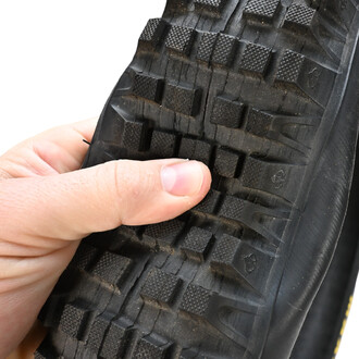 Pneu 20x2.5 Quax, vu de près, avec un fond noir et un motif de crampons sur la bande de roulement, tenu par une main.