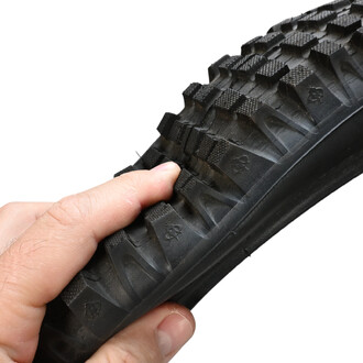 Pneu 20x2.5 cross Quax, tenu dans une main, montrant le profil avec une bande de roulement à la texture sculptée et un côté noir lisse.